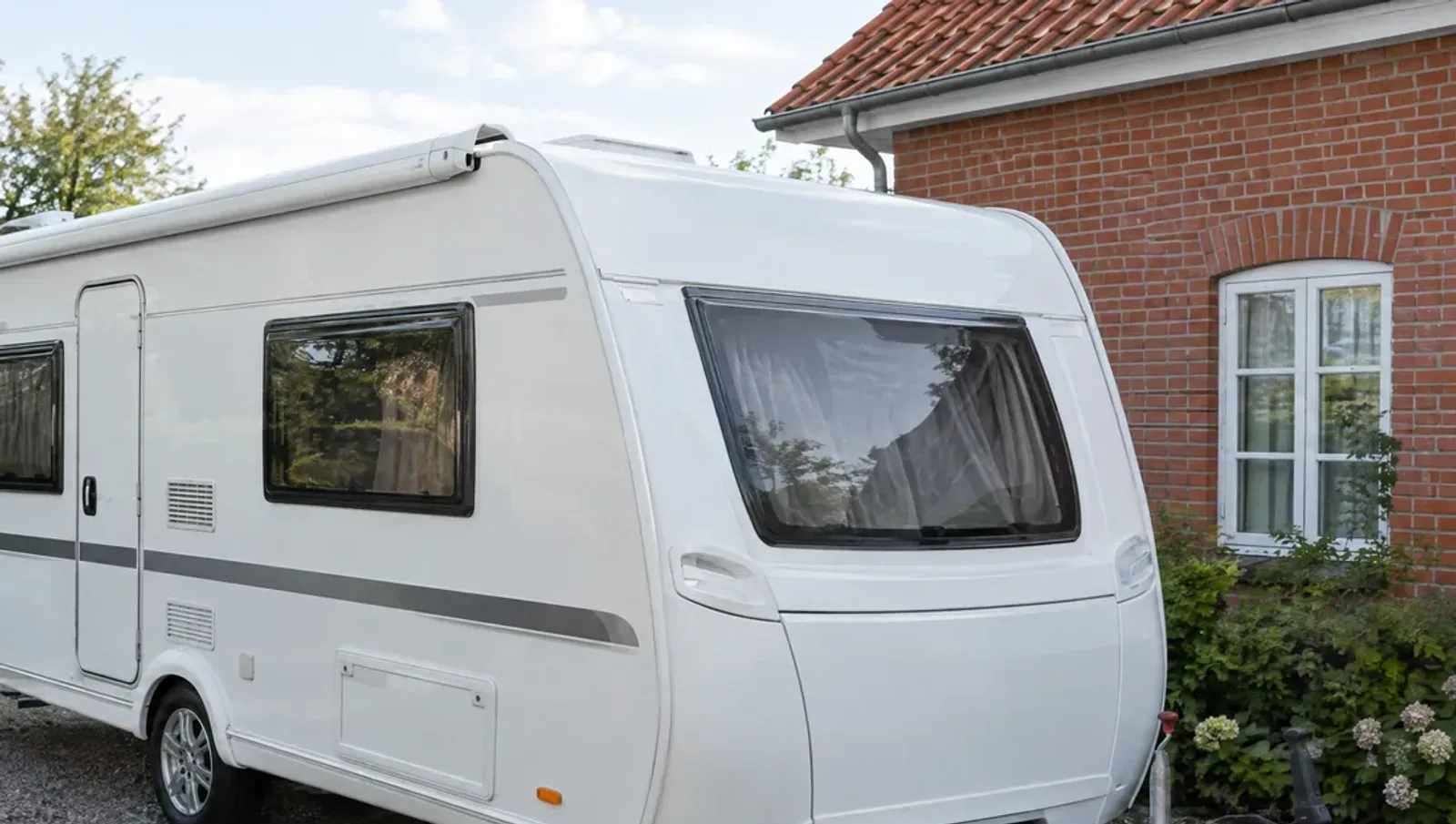 Hvid campingvogn set fra siden i en indkørsel med hjul og chassis i forgrunden